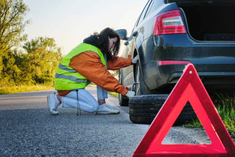 The girl changes the damaged wheel of the car