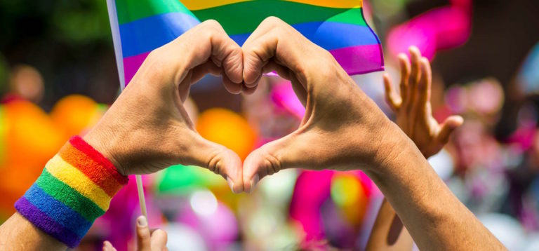 Hands making heart sign in front of rainbow flag