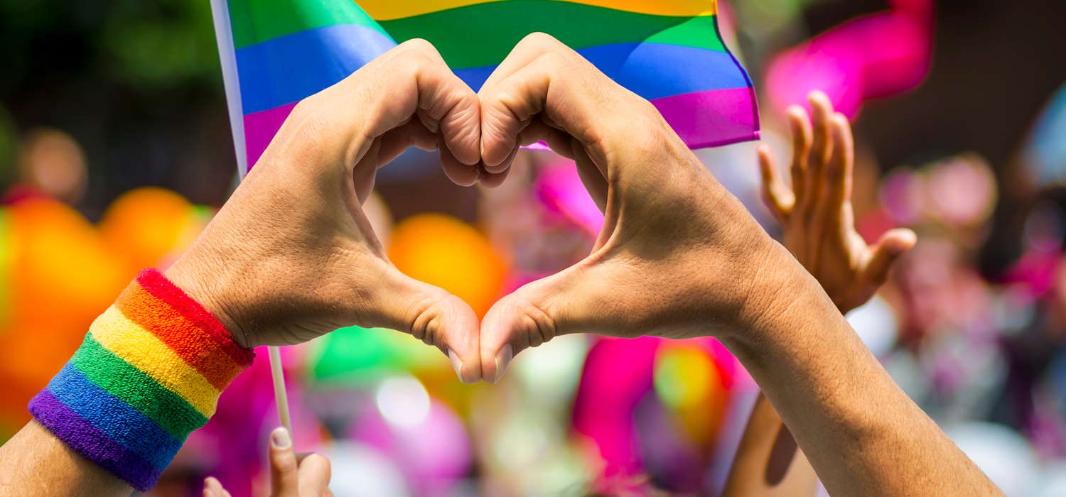 Hands making heart sign in front of rainbow flag